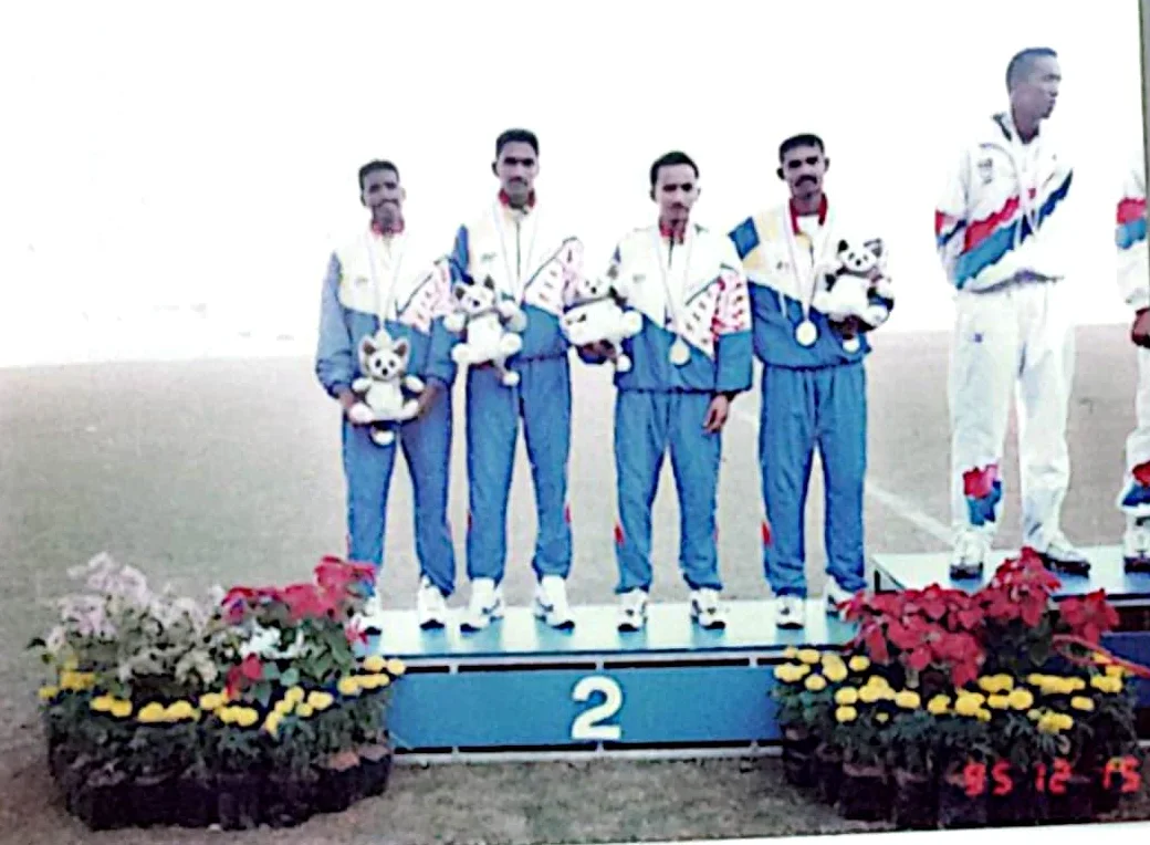 Four Malaysian athletes on the second-place podium at the 1995 SEA Games, silver medals round their necks and a Games mascot under one arm. The print carries the camera's date stamp, 95 12 15.